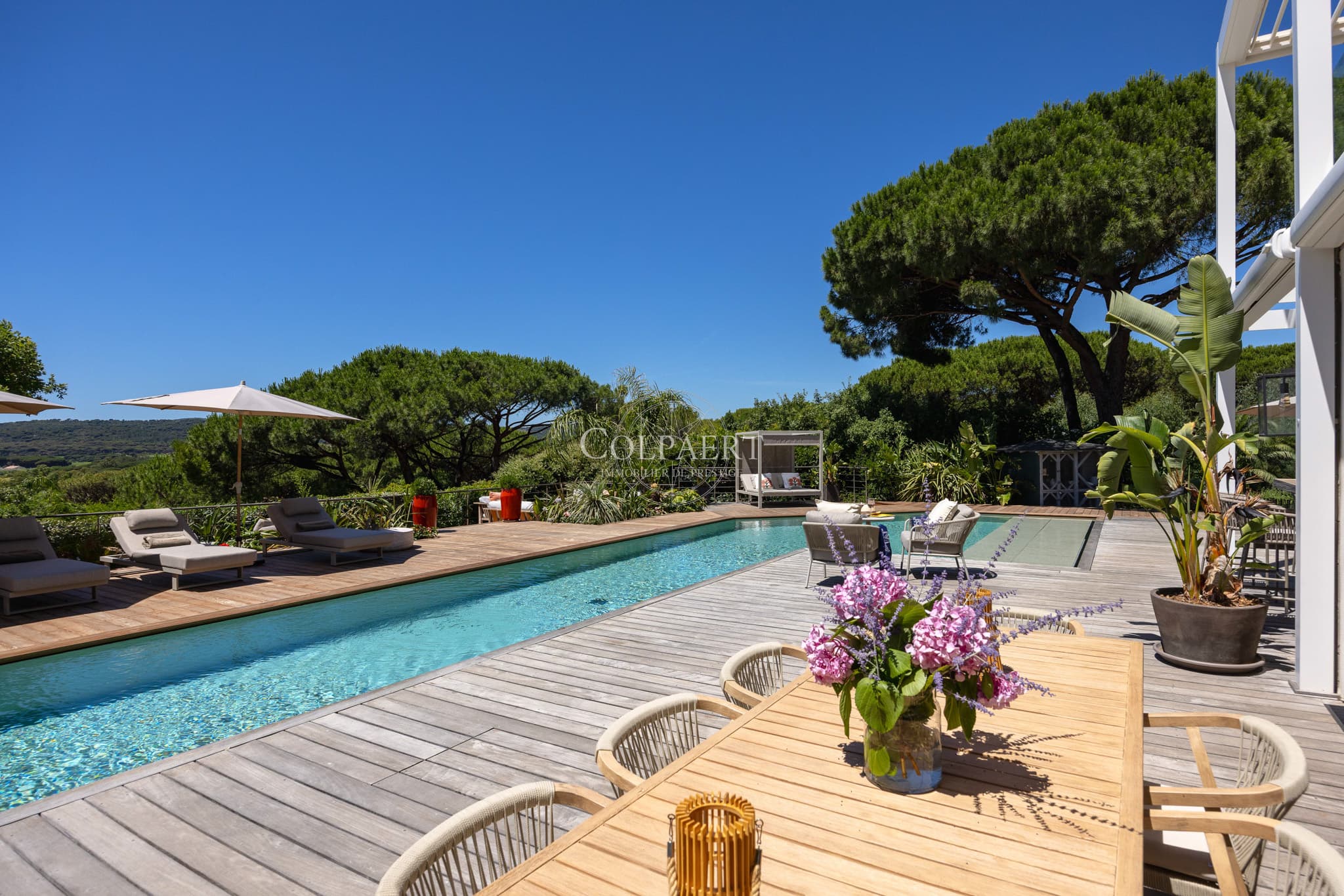 Terrasse ensoleillée offrant une vue dégagée sur la piscine et les jardins paysagers d'une propriété de prestige près des plages de Pampelonne.