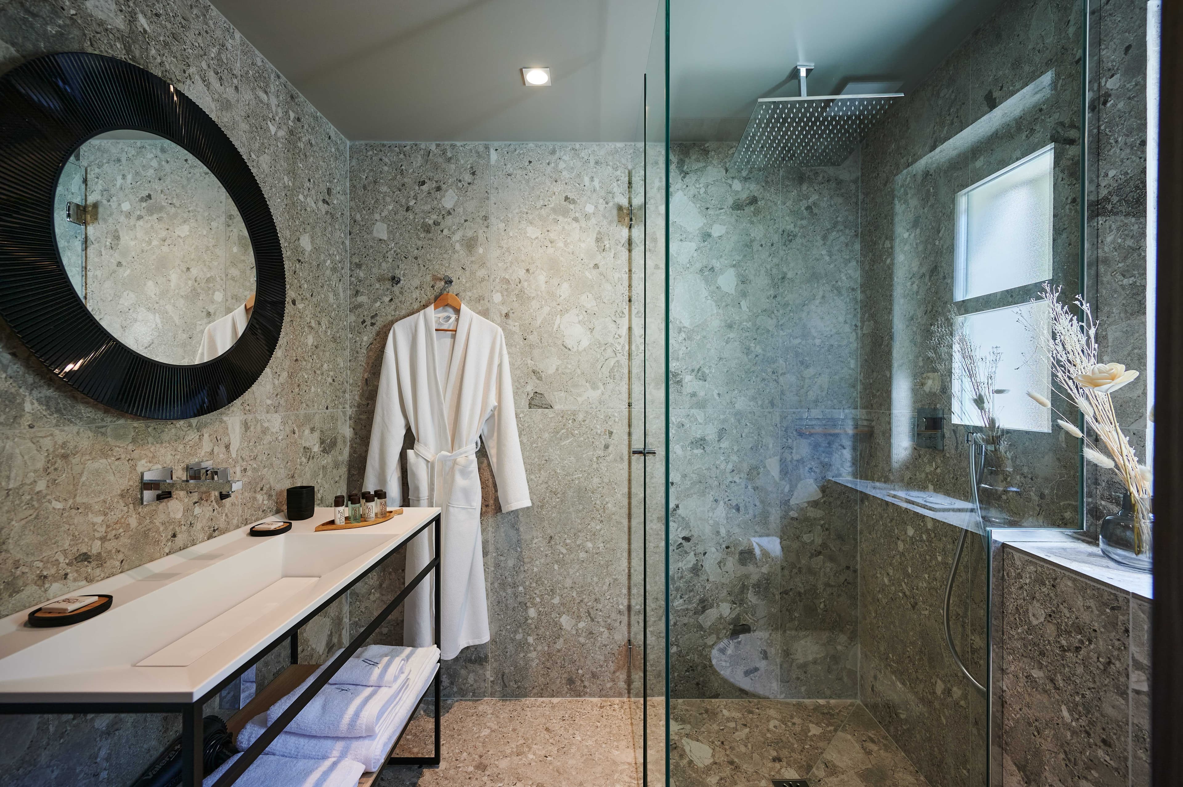 Salle de bains luxueuse en pierre naturelle avec douche à effet pluie dans une villa haut de gamme à Ramatuelle.