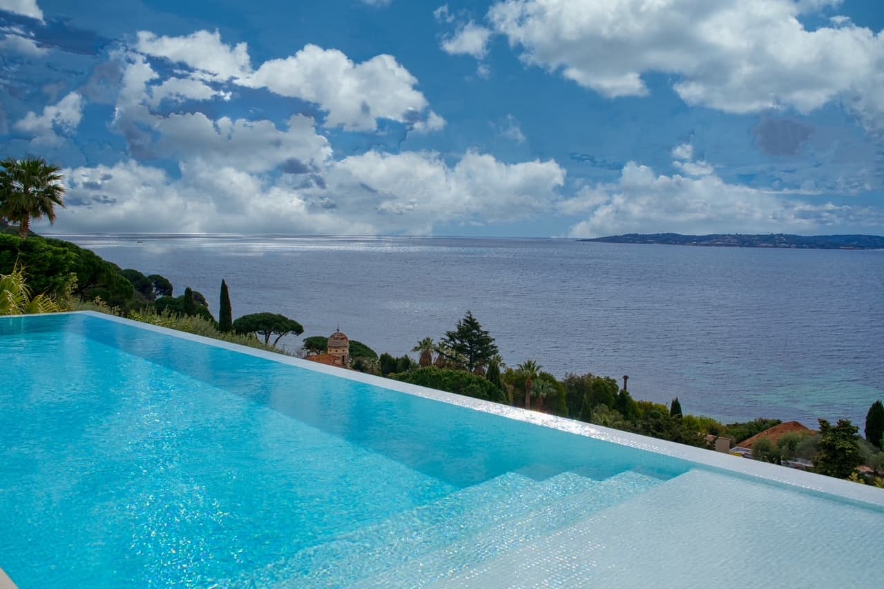 Piscine à débordement et solarium offrant un cadre idyllique face à la mer, dans une villa moderne de prestige.