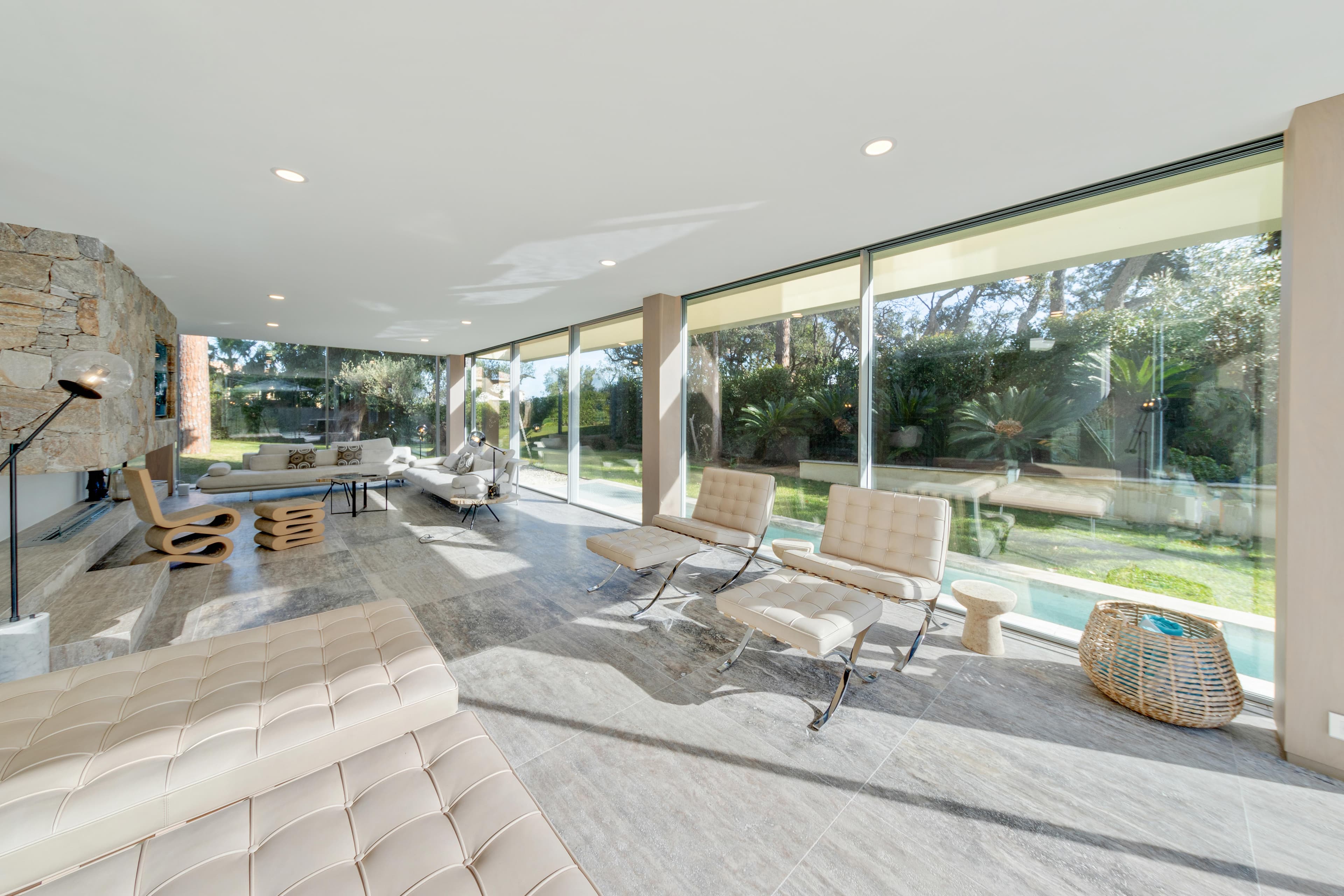 Vaste salon avec canapés et grandes baies vitrées ouvrant sur la terrasse. Villa moderne à vendre à Saint-Tropez.